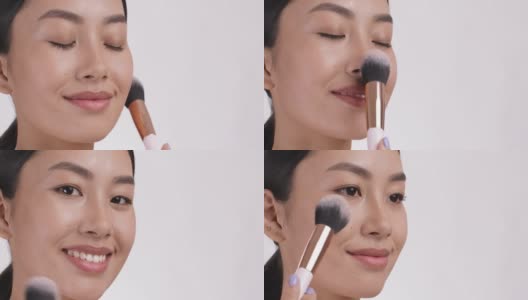 年轻的亚洲女士用化妆刷在脸上涂腮红。化妆概念，特写，白色工作室背景高清在线视频素材下载