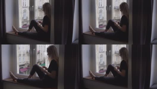 一个女人坐在窗台上，在家里使用智能手机的罕见景象高清在线视频素材下载