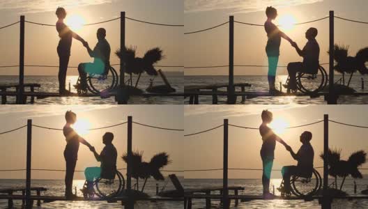 女性和男性残疾人的剪影在轮椅上抱着胳膊，在海上看地平线高清在线视频素材下载