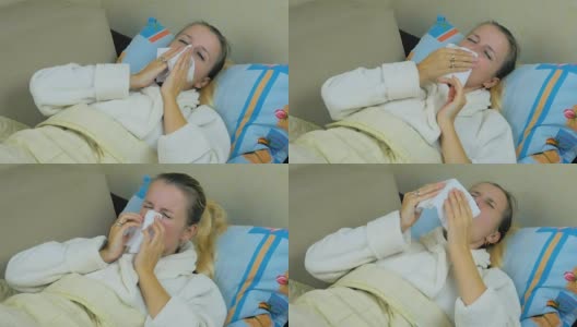 特写一个生病的年轻女孩在一个白色的罩衫打喷嚏和擦她的鼻子躺在沙发上。4 k。高清在线视频素材下载