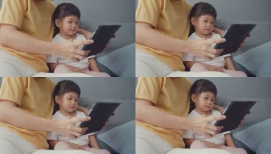 快乐快乐的亚洲家庭妈妈和可爱的孩子使用数字平板电脑兴趣卡通和看电影，在家里客厅的沙发上放松。高清在线视频素材下载