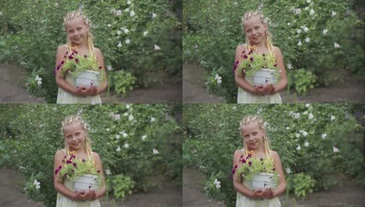 一个积极微笑的学龄女孩手里拿着花园里美丽的花朵。一个真正的孩子气的微笑。这个孩子从事园艺。高清在线视频素材下载