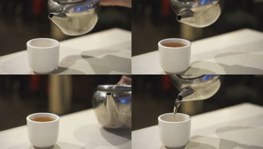 手将金属茶壶中的中国茶倒入瓷杯中高清在线视频素材下载