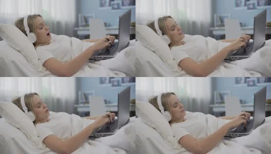 微笑的女孩躺在床上，用笔记本电脑在社交媒体上与朋友交流高清在线视频素材下载