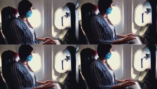 在一架飞机的机舱里，一个戴着防护面具的年轻女子，一名自由职业者在一台笔记本电脑上工作。工作和旅行的概念。新冠肺炎疫情后航班开通高清在线视频素材下载