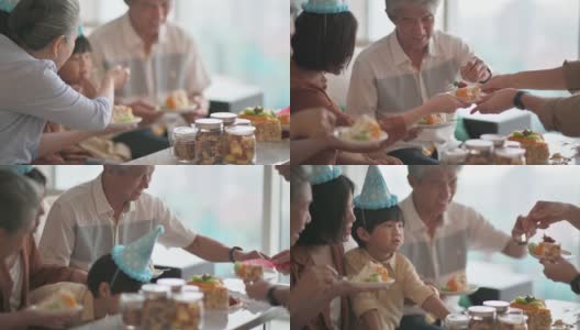 亚洲华人多代同堂庆祝生日，孙子戴着派对帽在客厅吃生日蛋糕高清在线视频素材下载