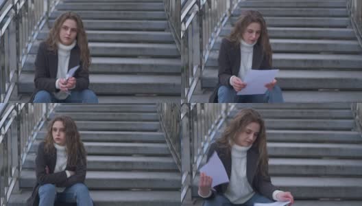 年轻的黑发白人悲伤的女人读信撕纸坐在城市的楼梯户外。压抑压抑愤怒的千禧年春日肖像秋日。缓慢的运动。高清在线视频素材下载