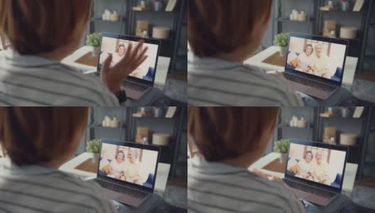 年轻的亚洲女孩使用笔记本电脑视频电话会议与年长的家庭爸爸和妈妈，而工作在家坐在客厅的沙发上。高清在线视频素材下载