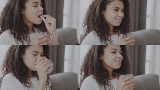 开朗的年轻非洲裔美国妇女吃药和在客厅内部的一杯水高清在线视频素材下载