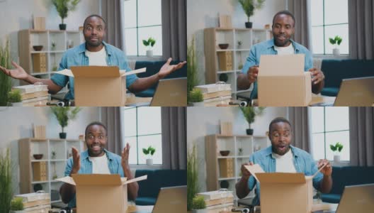 在打开纸箱时，坐在镜头前的可爱兴奋快乐的大胡子非洲裔美国人以惊讶的表情看着高清在线视频素材下载