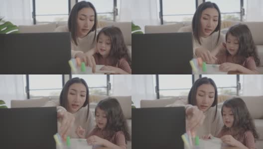 亚洲母亲帮助学龄前的女儿女孩在家里使用笔记本电脑电子学习，放大在线虚拟课堂，家庭教育，新常态的概念高清在线视频素材下载