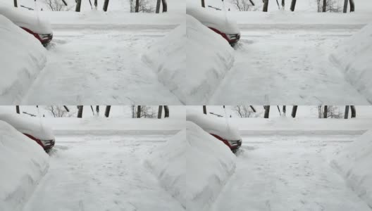 从一幢公寓楼的入口看出去，一辆被雪覆盖的红色汽车和巨大的雪堆高清在线视频素材下载