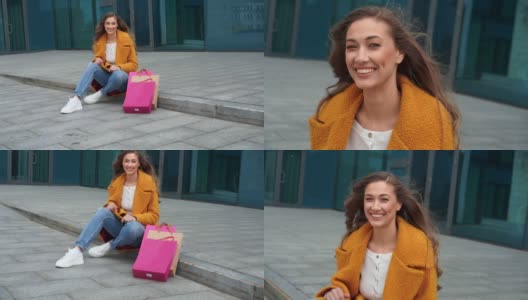 女商人拎着购物袋，身穿黄色外套，坐在公司大楼外面的地上高清在线视频素材下载