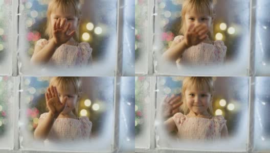 在平安夜可爱的小女孩透过白雪，冰冻的窗户看着和微笑。高清在线视频素材下载