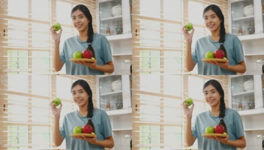 年轻的亚洲女人拿着苹果与幸福在家里的厨房，人们健康的生活方式高清在线视频素材下载