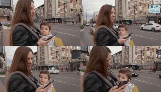 漂亮的年轻女子穿着黑色皮夹克和她的儿子在婴儿推车看她的智能手机和使用应用程序订出租车高清在线视频素材下载