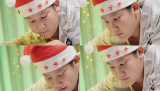 快乐的亚洲男孩戴着圣诞帽和看书和躺在床上在晚上的时间与圣诞装饰，生活理念。高清在线视频素材下载