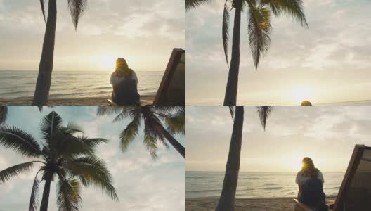 亚洲女人使用智能手机，坐在海边的海滩在早上日出的天空背景。独自快乐旅行的概念。4 k慢动作。高清在线视频素材下载
