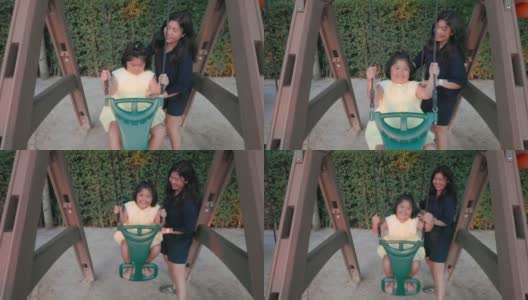 4K慢镜头:亚洲妈妈和可爱的女儿在公共游乐场开心地玩秋千。高清在线视频素材下载
