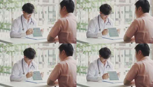 亚洲医生在诊所与病人交谈，同时使用平板电脑解释病人的情况和治疗结果。高清在线视频素材下载