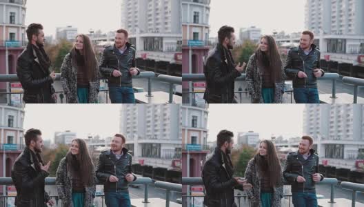 两个英俊的年轻人和一个漂亮的女孩在桥上聊天。朋友聊天笑笑，看路上的车。缓慢的莫高清在线视频素材下载