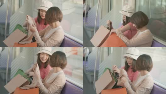 两个年轻的亚洲女人在地铁上展示她们在购物袋里买的新东西，慢镜头高清在线视频素材下载