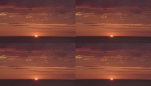 在明亮的红色和橙色的日落上，太阳在海洋的后面，很少有云高清在线视频素材下载