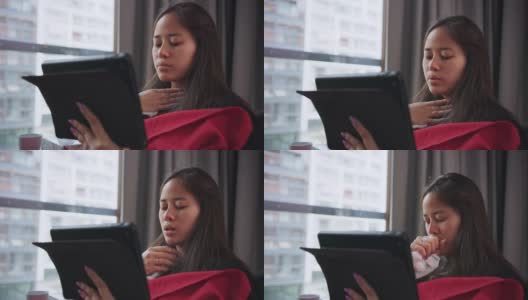 一个多病的年轻女子在用纸巾擤鼻子。坐在沙发上用笔记本电脑高清在线视频素材下载