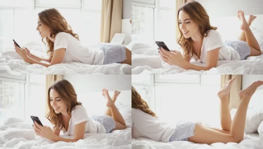 侧面的微笑黑发女人穿着睡衣躺在床上写信息在智能手机高清在线视频素材下载