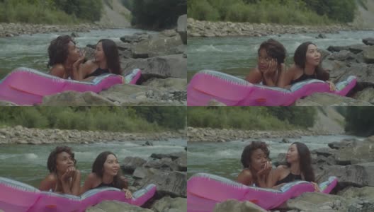 漂亮的多元文化女性朋友泳装享受在空气床垫在山河休闲高清在线视频素材下载