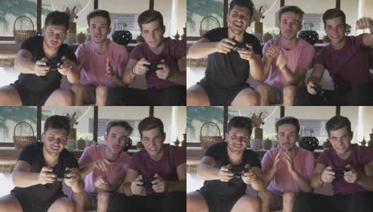 帅哥们坐在休息室的沙发上一起玩网络游戏，用操纵杆享受团队胜利高清在线视频素材下载