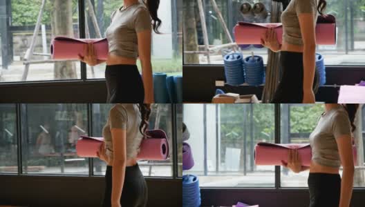 亚洲女子手拿瑜伽垫来上瑜伽课。健康、城市生活方式理念。慢动作镜头。高清在线视频素材下载
