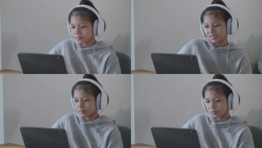 一个亚洲女孩晚上戴着耳机在平板电脑上通过网络学习。亚洲女孩的在线学习理念是戴着耳机在平板电脑上通过互联网进行在线学习。在家在线学习的概念高清在线视频素材下载