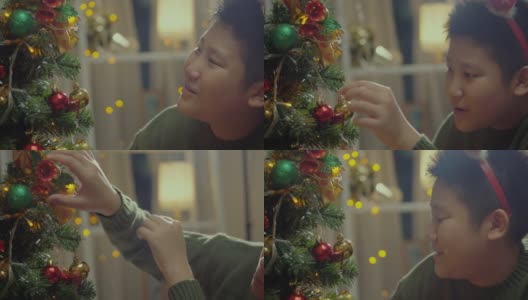 快乐的亚洲男孩穿着绿色的毛衣和红色的发带装饰圣诞树在晚上的时间在家里，节日的概念。高清在线视频素材下载