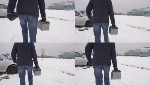 一个男人携带并安装了一个汽车电池在汽车里，冬天。雪,慢动作高清在线视频素材下载