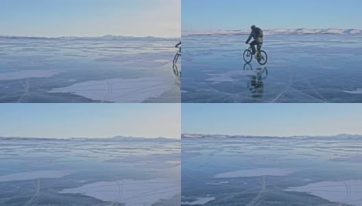 男人在冰上骑自行车。骑自行车的人穿着灰色羽绒服，背着背包，戴着头盔。结冰的贝加尔湖的冰。自行车的轮胎上覆盖着特殊的尖钉。高清在线视频素材下载