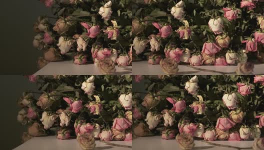 一束枯萎的粉红色玫瑰花。暗室里的桌子上放着干玫瑰高清在线视频素材下载