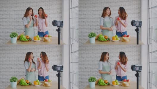 两个年轻的亚洲女性美食博主拿着红苹果，一边讲解健康的食物和健康的生活方式，一边录制视频播放，Vlog健康的生活方式高清在线视频素材下载