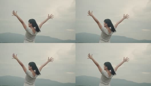 年轻的亚洲女子在运动服装高举在空中的山景感觉幸福。高清在线视频素材下载