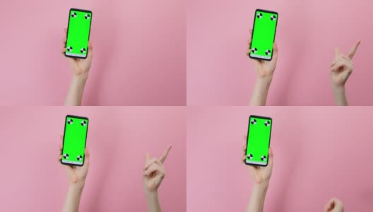 一位女性的手拿着一部带有垂直绿色铬合金屏幕的智能手机，并掰着手指。粉红色的背景。智能手机应用程序的概念高清在线视频素材下载