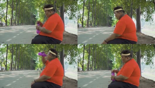 一个胖子坐在公园里喝水高清在线视频素材下载