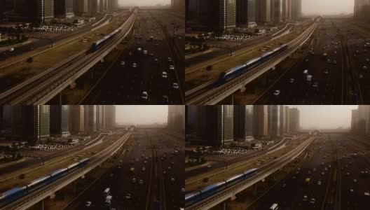 从空中俯瞰蓝色的高速列车，它穿过高速公路上的立交桥，汽车被摩天大楼包围。迪拜,阿联酋高清在线视频素材下载
