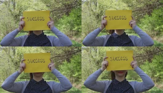一个年轻的女人拿着一张黄色的纸，上面写着成功高清在线视频素材下载