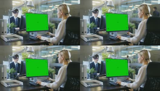 在办公室里，女商人在她的办公桌前对着一台模拟的绿色屏幕的个人电脑工作。同事走进办公室，并在他的办公桌前发生。高清在线视频素材下载