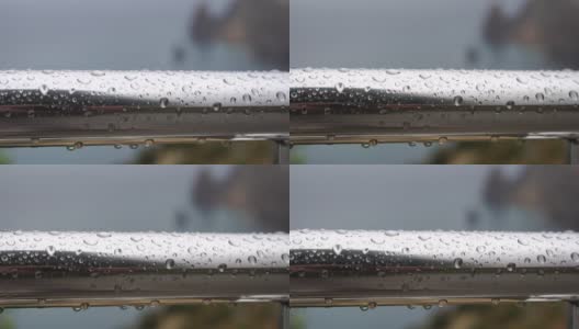 不锈钢扶手上的雨滴映衬着模糊的大海背景。特写镜头。雨露的水滴聚集在闪闪发光的铬钢杆扶手上高清在线视频素材下载