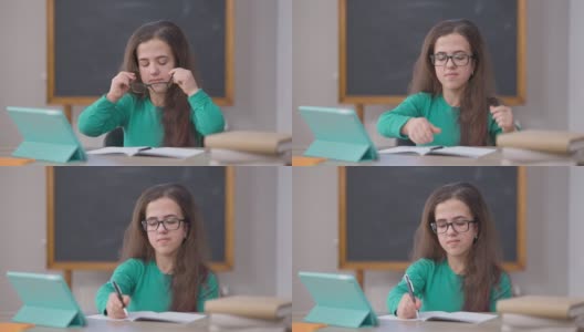 天才集中肖像白种年轻女子戴着眼镜，看着平板电脑屏幕写字，坐在书桌前。聪明自信的小个子在室内在线学习。高清在线视频素材下载