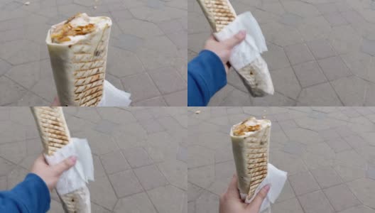人手握长烧烤多汁包装在塑料袋沙瓦玛与餐巾纸对街道灰色鹅卵石的特写高清在线视频素材下载
