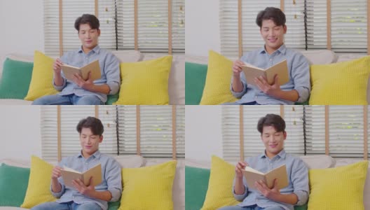 快乐英俊的亚洲男人坐在沙发上微笑和阅读书籍放松时间在家里。兴高采烈的商人穿着蓝色衬衫，坐在沙发上看书高清在线视频素材下载