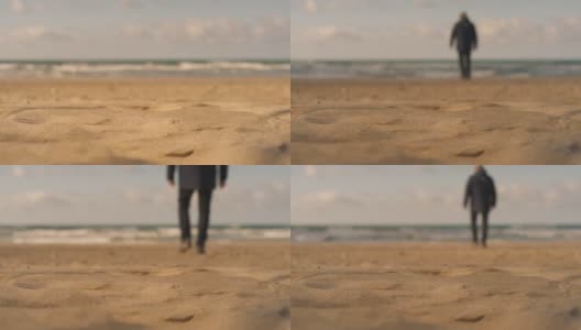 一个男人的剪影走在海边的沙滩上，离开了镜头。平静的海边漫步，模糊的背景，浅景深4K直播视频。蓝天白云，春日艳阳高清在线视频素材下载