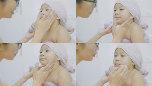 母亲在浴室里给女儿脸上擦面霜高清在线视频素材下载